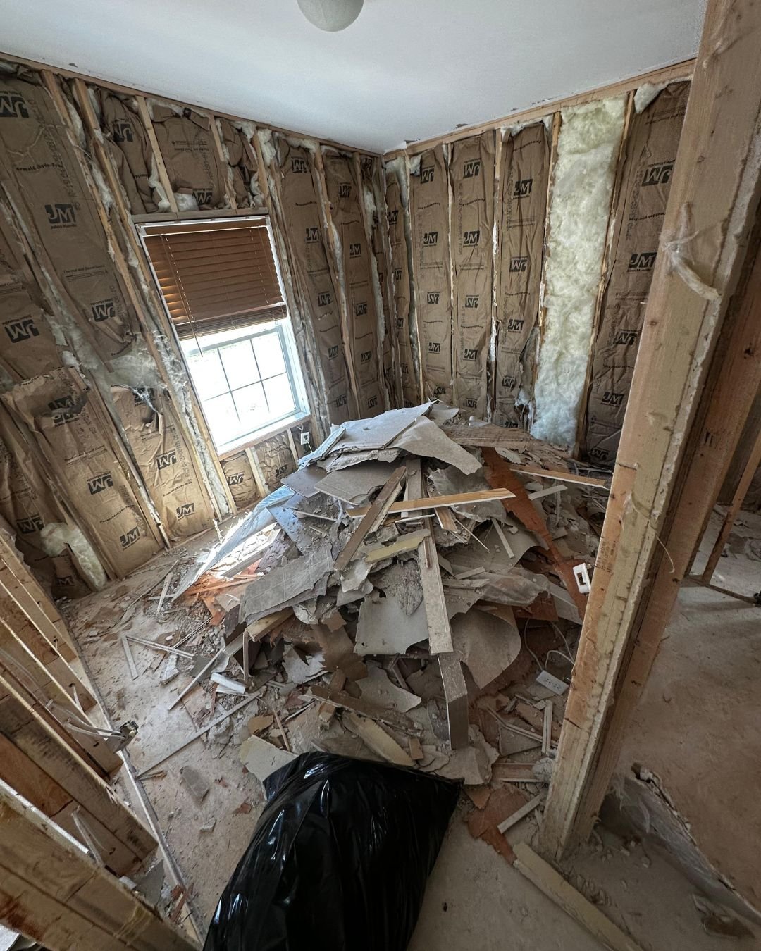 nterior room down to studs with insulation exposed, a large pile of broken drywall and wood debris covering the floor, and a black contractor bag in the foreground