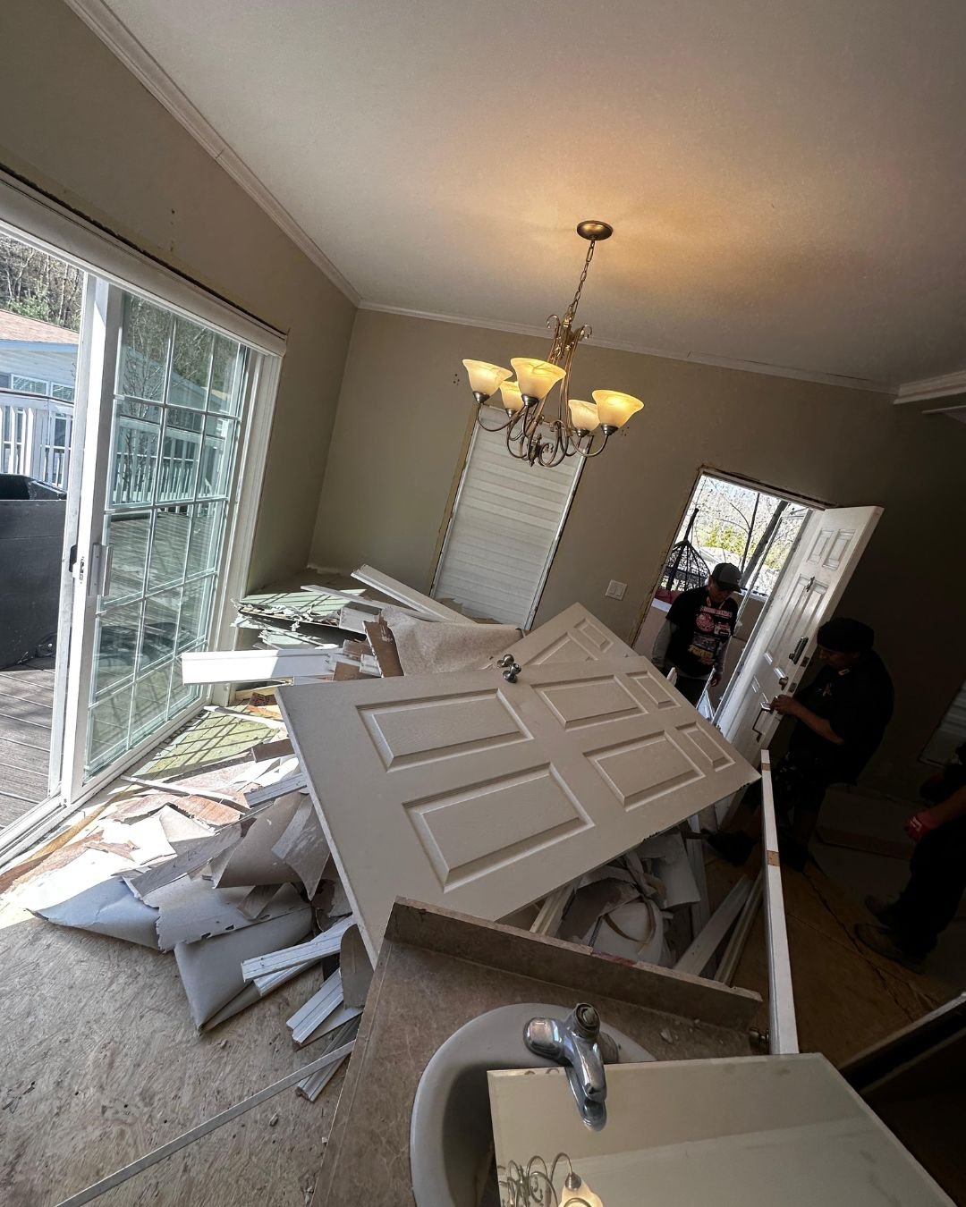 A pile of demolition waste and old white doors on a residential floor, next to a newly installed bathroom vanity with a chrome faucet.