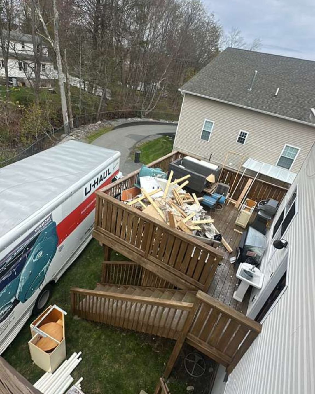 Aerial view of a dramatic junk removal project, showing a massive pile of construction debris and wood planks on a deck, with a large U-Haul moving truck parked right next to the stairs for quick loading